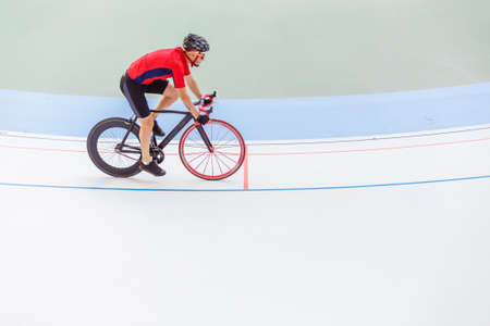 Racing cyclist on velodrome outdoor. Professional athlete in a red T-shirt and a black bicycle.の写真素材
