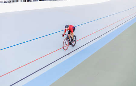 Racing cyclist on velodrome outdoor. Professional athlete in a red T-shirt and a black bicycle.の写真素材