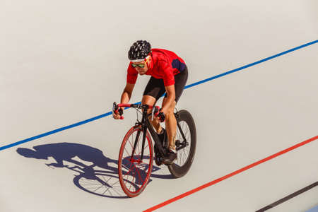 Young professional cyclist on a velodrome. Sports man in a red T-shirt and a black bicycle.の写真素材