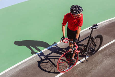 Athlete with a black bicycle at velodrome. Professional sports man in a red T-shirt and helmet.の写真素材
