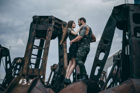 Man in khaki clothing and tattoos hugging the young woman at the rusty elements. Couple of young people in love on city of urban background.の写真素材