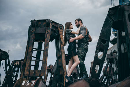 Attractive young couple wearing in stylish fashion clothes. Man and a woman embrace on a rusty pile of metal.の写真素材