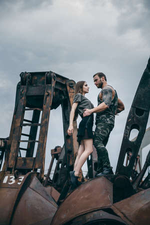 Man and a woman embrace on a rusty pile of metal. Young man and woman in passion emotions of the street on city of urban background.の写真素材