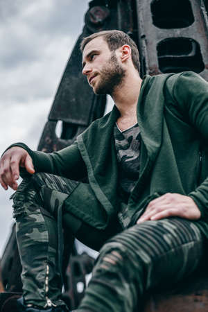Portrait of a young handsome bearded man, model of fashion, in clothes khaki colors. Man on city of urban rusty background.の写真素材