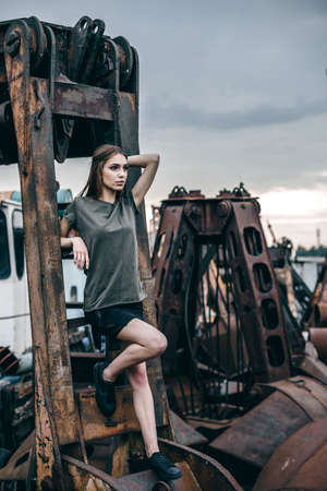 Stylish fashion portrait of trendy casual young model on a metal rusty detail. Trendy beautiful long haired model posing on a rusty pile of metal background.の写真素材