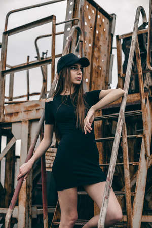 Beautiful and fashion young woman posing on the steps of rusty metal. Portrait of a young woman, model of fashion in urban background.の写真素材