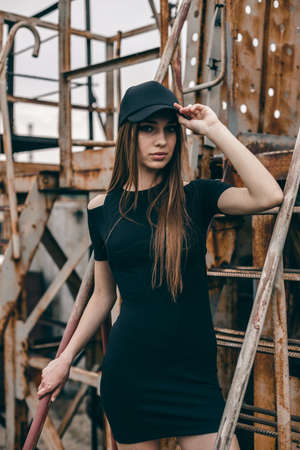 Young girl in a black dress and cap on a city urban background. Metal rusty ladle of an abandoned factory.の写真素材