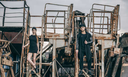 A beautiful fashionable couple stands on metal rusty stairs. Metal rusty ladle of an abandoned factory.の写真素材