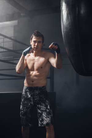 Active man with boxing wraps training punch for punching bag. Young man doing boxing workout in the gym.の写真素材