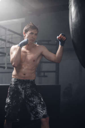 Young man doing boxing workout in the gym. Male fighter smash punching bag.の写真素材