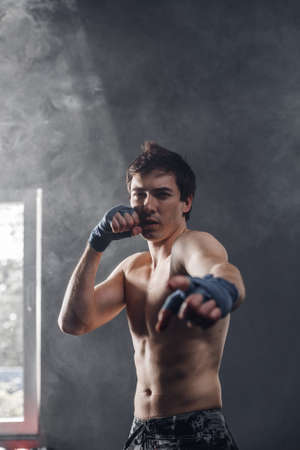 Boxer in the sun and smoke training hands with boxing wraps. Muscular strong man on background boxing gym.の写真素材