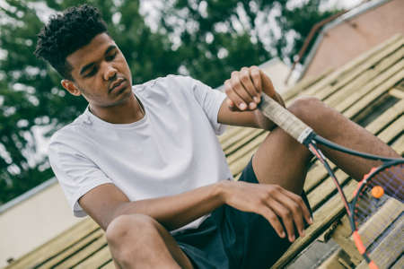 Close-up of a tennis player holding a racket sitting on a bench. The sportsman has a rest from below.の写真素材