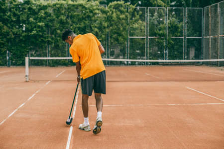 A young man in a sports uniform is cleaning a tennis court. The tennis player is preparing a court for the game.の写真素材