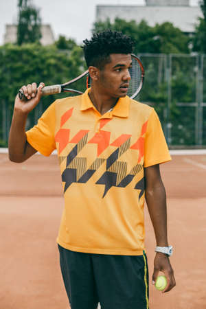 Portrait of a confident tennis player standing on tennis court. Handsome young man in polo shirt holding tennis racketの写真素材