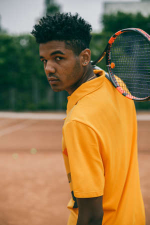 Portrait of serious african man holds a tennis racket on his shoulder. Back view portrait of a man playing in tennis outdoors.の写真素材