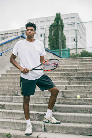 Tennis is his passion. Confident young man in sports clothes carrying tennis racket and looking away while standing against grey background.の写真素材