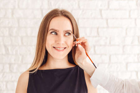 The beautician makes natural beautiful eyebrows. The model is smiling and looking at the camera.の写真素材