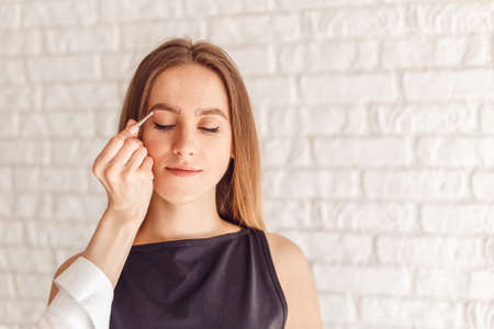 Portrait of a model and the masters hand with tweezers. Young woman tweezing her eyebrows.の写真素材