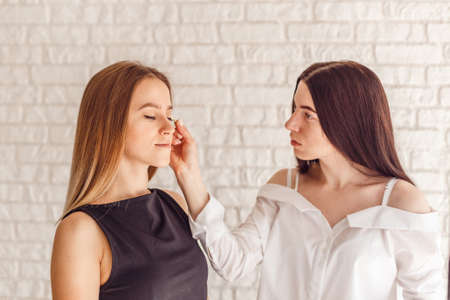 Beautiful young woman gets eyebrow correction procedure. Young woman tweezing her eyebrows in beauty saloon. Young woman plucking eyebrows with tweezers close upの写真素材