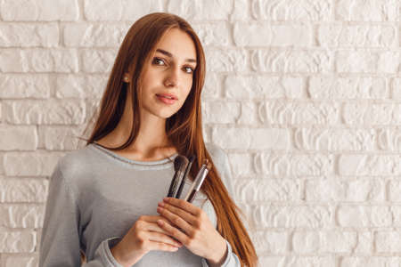 Closeup portrait of smiling sexy female model in beauty salon with tassels for make-up in hands. Beautiful young woman with nude face makeupの写真素材