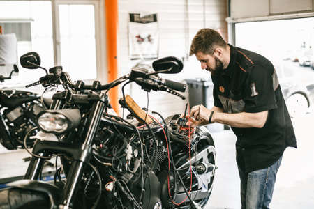 Professional motorcycle mechanic working in bike repair service. Mechanic checking a bike battery level with voltmeter in garageの写真素材