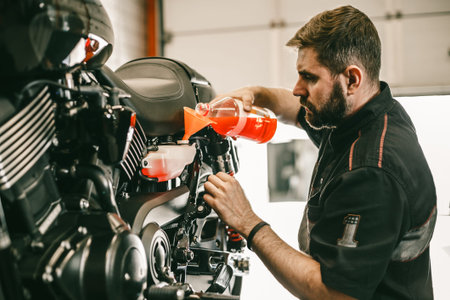 Professional mechanic pouring antifreeze into a motorcycle. Confident young man repairing motorcycle...
