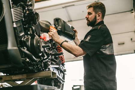 Motorcycle mechanic replacing and pouring fresh oil into engine at maintenance repair service station. Portrait of an auto mechanic putting oil in a car engine.の写真素材