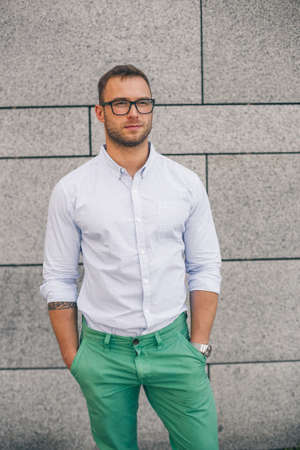 Cheerful smiling young male model in glasses. A handsome man in green trousers stands on the background of a concrete wall.の写真素材