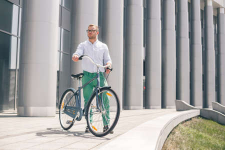 Handsome hipster enjoying city ride by bicycle. Businessman and his bicycle on city streets. The concept of the modern lifestyle of young men.の写真素材