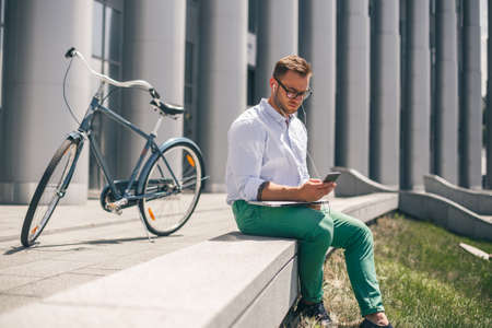 Serious young man in headphones working on laptop while sitting at outdoor of office. Good music increases productivity.の写真素材