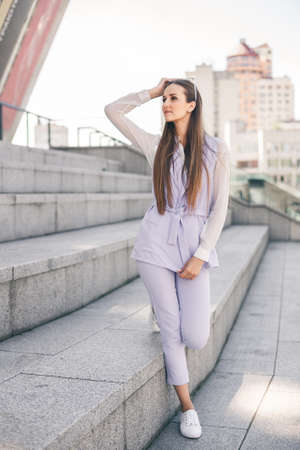 Beautiful young woman in a business purple suit against a city background. Female office worker stands on concrete steps.の写真素材
