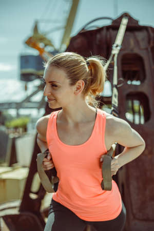 Close-up portrait of an athlete in uniform during exercise with TRX exercise outdoors. Beautiful young woman in an orange T-shirt.の写真素材