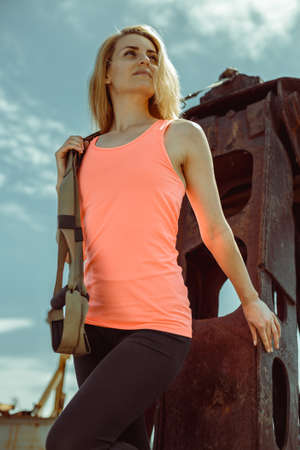 Blonde fitness woman posing with trx fitness straps on metal rusty surface. Beautiful muscular woman doing exercise with trx system.の写真素材