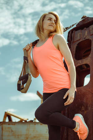 Beautiful muscular woman with trx system outdoor city urban. Blonde fitness woman posing with trx fitness straps.の写真素材
