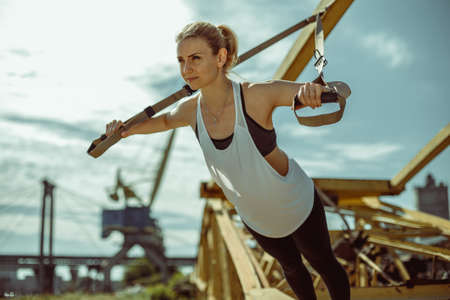 Young attractive woman does suspension training with fitness straps outdoors in the nature.の写真素材