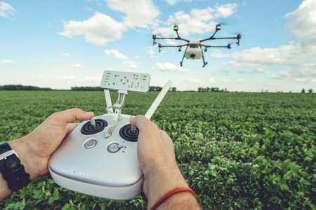 The man control octocopter or remote control for the drone in the hands for take a picture on sky. Agriculture drone flies over the green field.の写真素材
