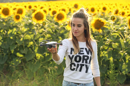 Portrait of a beautiful woman holding a mini drone on her hand. The girl stands against the background of a field of sunflowers. Dron is preparing to take off.の写真素材