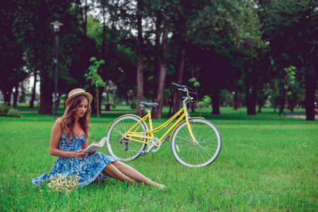 Young female relaxing on a green grass with bicycle in a park on a sunny day. Pretty female university student take a break outdoors, countryside.の写真素材