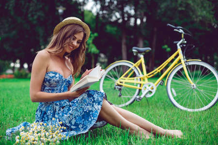 Beautiful young woman portrait reading a book with bicycle in the park. Relax intellectual cycling fitness nature outdoor concept.の写真素材