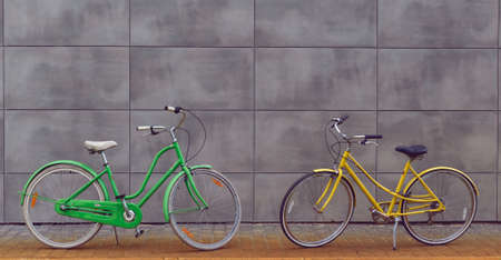 Two urban female bicycles on a gray wall background. Green and yellow bikes. Active lifestyle.の写真素材