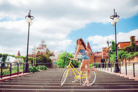 Amazing woman posing near bicycle, fashion model in sexy clothes. Sexy model with a yellow grand on the background of the city.の写真素材