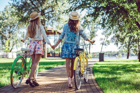 Women walking in the summer park holding hands looking in the sunset with their bikes. Active lifestyle concept.の写真素材