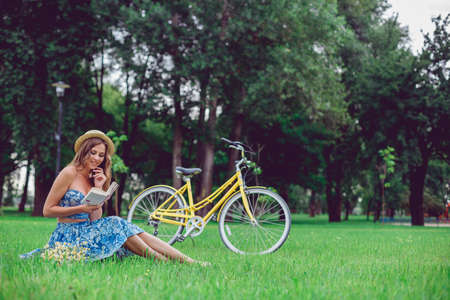 Young female relaxing on a green grass with bicycle in a park on a sunny day. Pretty female university student take a break outdoors, countryside.の写真素材