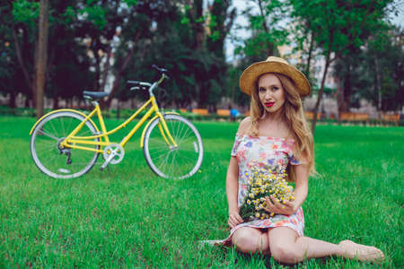 Outdoor portrait of a beautiful blonde woman. Attractive sexy girl in a field with flowers and bike on the background.の写真素材