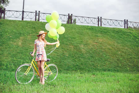 Beautiful young woman on a bicycle on a green lawn background. Summer lifestyle and active rest. Yellow bicycle and balloons.の写真素材