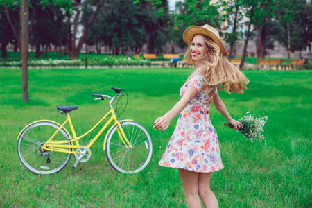 Beautiful happy young woman enjoying summer with wild-flower bunch. Happy girl dancing outdoor, relaxation and good mood in park, sunset. Bicycle on the background.の写真素材