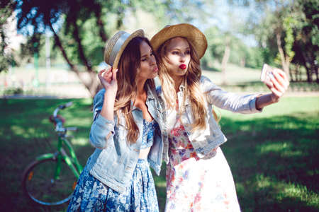 Female friends taking selfie at a national park. Young women posing, bicycles stand in the background.の写真素材