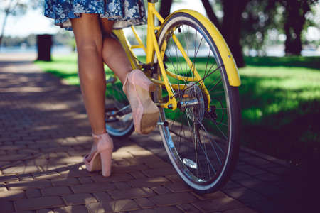 Close-up of female legs in summer boots and yellow bicycle retro wheel. Yellow bike and beautiful female legs.の写真素材