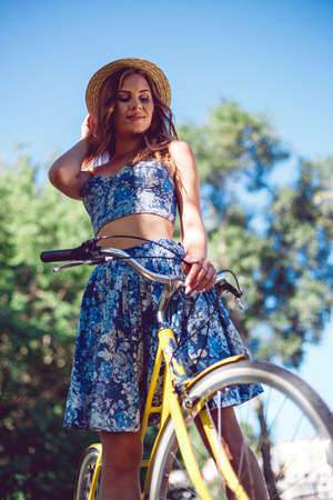Closeup portrait of smiling young caucasian woman and the wheel of a bicycle. Cheerful young woman enjoying a dawn in the park.の写真素材