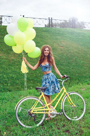 Young sexy woman in blue dress with balloons and retro bicycle posing in the parkの写真素材